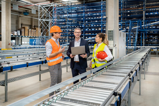 Blue-collar workers discussing over laptop with businessman in warehouse