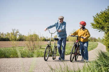 Happy grandfather and granddaughter walking with bicycle on road