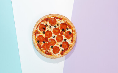 Italian pizza with pepperoni and olives on coloured background. Pepperoni pizza in minimal style on purple and blue colours. American pizza delivery concept with color backdrop