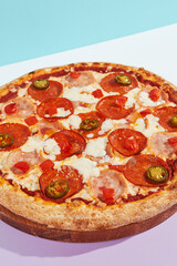 Italian pizza with ham, pepperoni and jalapeno on coloured background. Meat pizza with salami and chilli pepper in minimal style on blue color. American pizza delivery concept with color backdrop