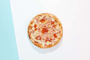 Italian pizza with ham and bacon on coloured background. Meat pizza with bacon and ham in minimal style on blue and orange color. American pizza delivery concept with color backdrop