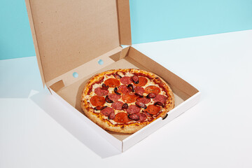 Italian pizza in paper box on coloured background. Meat pizza with sausage and salami in delivery...