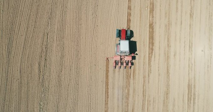 Drone aerial shot of a farmer in tractor seeding, sowing agricultural crops at field