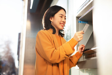 Happy smiling young woman withdrawing money from credit card. Young woman using ATM machine