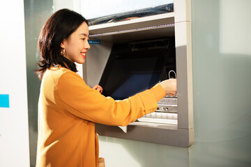 Fototapeta na wymiar Happy smiling young woman withdrawing money from credit card. Young woman using ATM machine