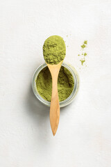 Ground green matcha or moringa tea powder. A jar of powder and a wooden spoon.