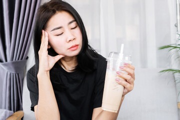 Asian woman having a headache and dizzy after drinking ice coffee, headache triggered by caffeine concept