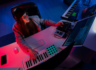 Beautiful caucasian girl in stylish clothes works in a recording studio with neon light in a cap...