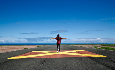 young brunette woman walking down the center of a runway with her arms raised with blue sky - 504873237