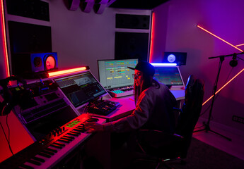 Beautiful caucasian girl in stylish clothes works in a recording studio with neon light in a cap...