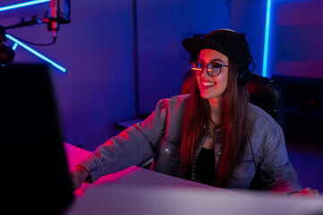 Beautiful caucasian girl in stylish clothes works in a recording studio with neon light in a cap...