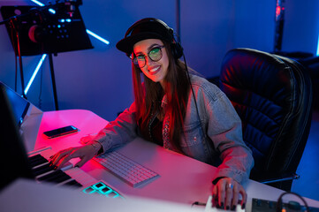 Beautiful caucasian girl in stylish clothes works in a recording studio with neon light in a cap...