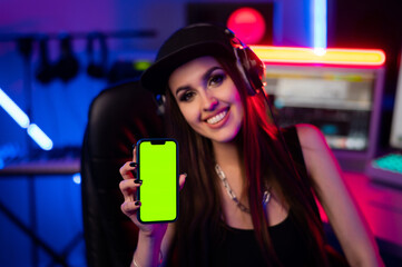 Beautiful caucasian girl in stylish clothes holding a phone with a green screen on a background of...