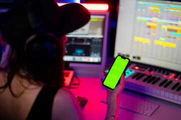 Beautiful caucasian girl in stylish clothes holding a phone with a green screen on a background of...