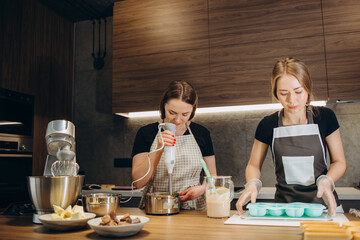 Beautiful friends in aprons prepare sweets in the kitchen of their own home