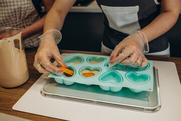 Chef pastry in a black apron filling the dough into a cupcake silicone mold on dark background....