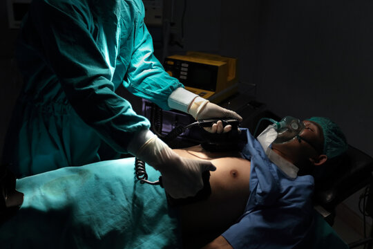 Closeup image of professional concentrated surgical team performing CPR with defibrillator on patient in hospital operating room or emergency room. Surgery concept