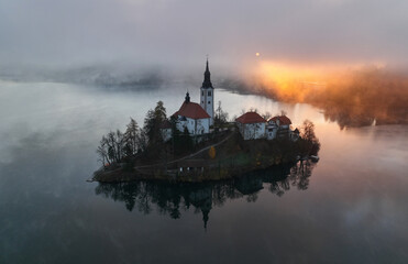 Lake Bled on a foggy and misty autumn morning. Vivid sunrise on a beautiful autumn day.