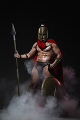 A young athletic man dressed as a Roman soldier in a red cloak stands with a spear in hand and a...