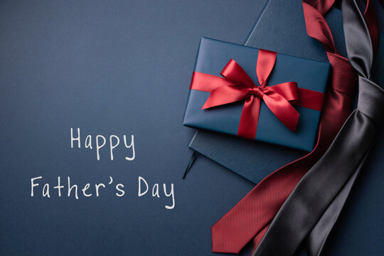 Happy Father's Day card with blue gift box, notebook and neckties on dark blue background.