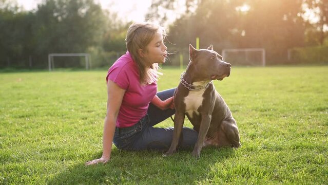 Sitting on the grass and having a rest. Young woman is on the walk with her pitbull dog outdoors