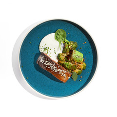 Roast salmon with crispy skin, grilled vegetables and espuma. Grilled salmon fillet with broccoli, avocado and white sauce. Keto food - baked fish with skin and green vegetables on white background.