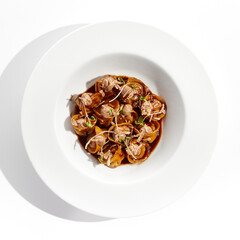 Main course in italian cuisine - meat tortellini with demi-glace sauce and mushroom cream. Beef ravioli on white plate. Tortellini with minced veal in beef sauce. Gourmet cuisine in restaurant menu.