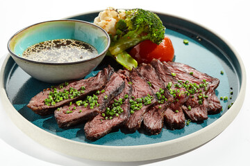 Roast beef with vegetables and sauce on trendy plate. Sliced meat steak roast grill with tomatoes and broccoli isolated on white table. Angus roast beef in healthy style for restaurant.