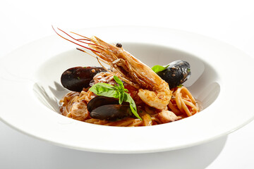 Italian dish - seafood linguine isolated on white background. Pasta with prawn, mussels, octopus,  squid in tomatoes marinara sauce. Seafood pasta in Italian restaurant menu. Seafood on white plate
