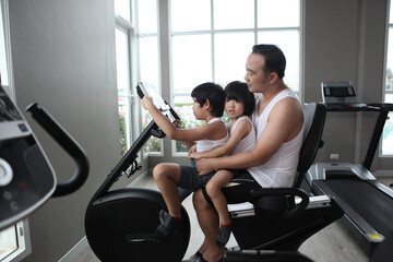 Fototapeta na wymiar Father and two son in the gym. Father and son spend time together and lead a healthy lifestyle. exercise bikes together.