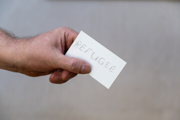 Refugee. A man's hand holds a white paper rectangle with text. A refugee is a person who has been...