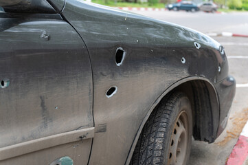 A passenger car with through holes from shrapnel standing in the parking lot. Damaged sedan during...