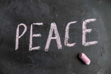 Peace. A word is written in pink chalk on a black chalkboard. Handwritten text. A piece of colored chalk hangs next to it.