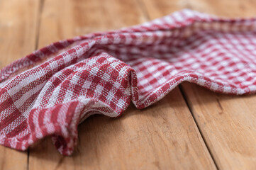 A red plaid kitchen towel lies on the countertop of a wooden table. Crumpled Towel or kitchen napkin on rough boards. Close-up. Selective focus.