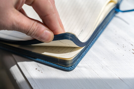 A man's hand holds an open notebook. Blue hardcover notebook with blank pages. Selective focus.