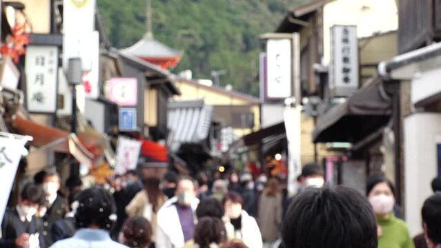 KYOTO, JAPAN - DEC 2021 : Back shot and crowd of people wearing masks to protect from Coronavirus (Covid-19). Tourists around Kiyomizudera (Kiyomizu Temple) in autumn leaves season. Slow motion shot.