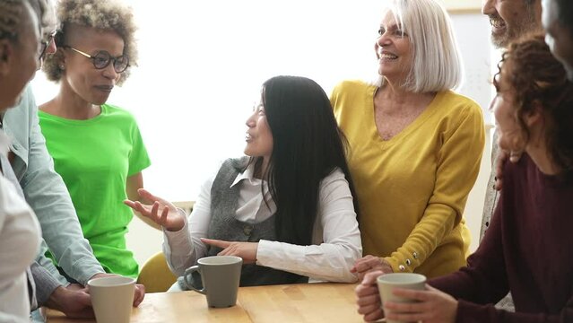 group of happy multiracial people of different ages talking in the kitchen, having fun having a cup of coffee at home