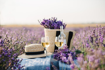 Two glasses with white wine and bottle on background of a lavender field. Straw hat and basket with...