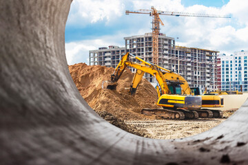 Heavy excavator at the construction site. View of the excavator through the iron pipe. Construction equipment for earthworks. Quarry excavator.