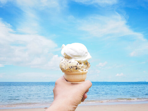 hand holding ice cream over summer beach background.