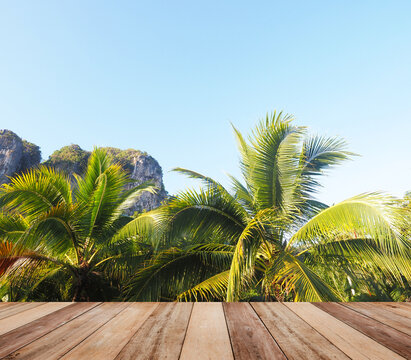 Wooden table top over coconut tree leaves and clear light blue sky