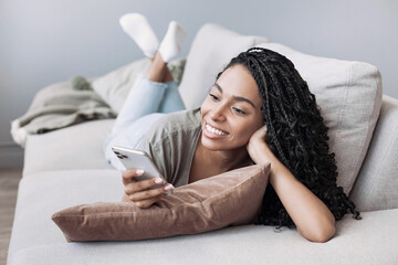 Young woman resting at home with smartphone, beautiful girl looking at phone laying on sofa, Online...
