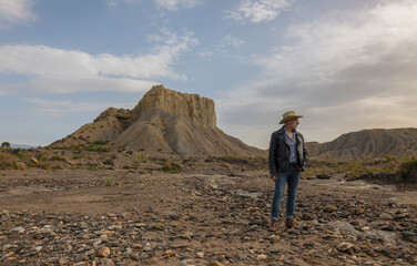Fototapeta premium Adult man in cowboy hat in desert against rock and sky
