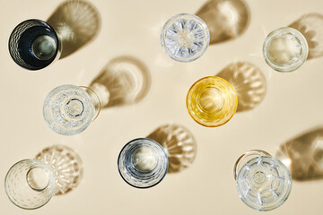 Overview of assortment of glasses of different colors with clean water standing on table or pastel...