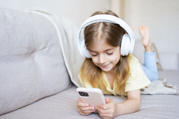 child with a phone is lying on the sofa with headphones watching cartoons, listening to music, playing games, talking on the phone.