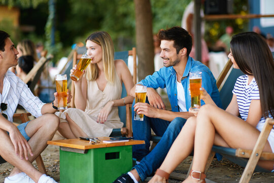 Group of young people sitting in a summer cafe drink beer and chat