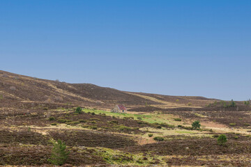 A scenic view of a Scottish moutain bothy in a valley  with moorland, grass and mountain summit under a beautiful blue sky