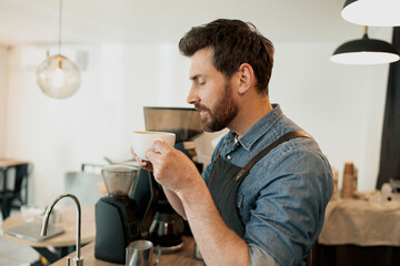 Handsome male barista holding cup of coffee and enjoying aroma of hot beverage