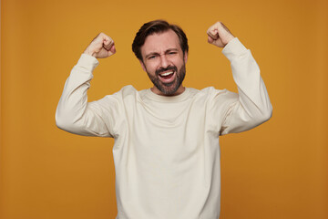indoor portrait of man wears white sweatshirt posing over yellow background smiles broadly, raised...