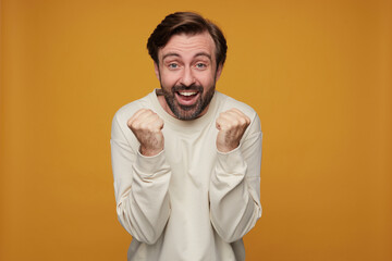 indoor portrait of man wears white sweatshirt posing over yellow background smiles broadly, raised...